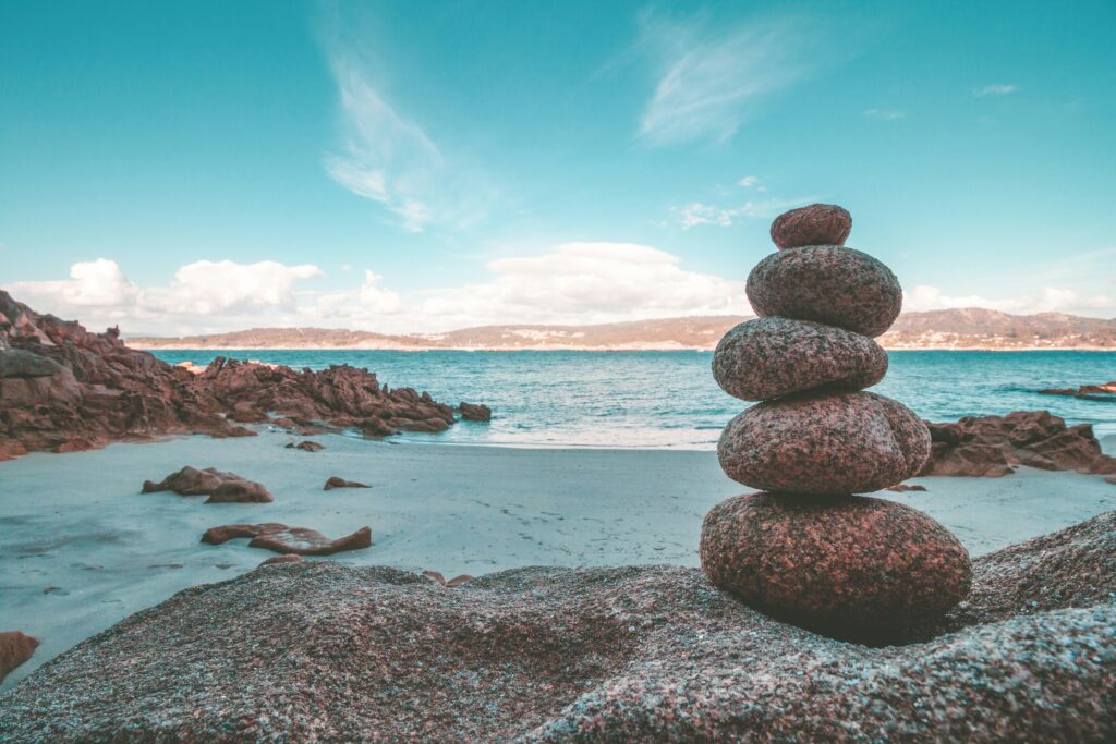 Rocks stacked on a beach representing mindfulness. Photo by Alejandro Piñero Amerio on Unsplash.