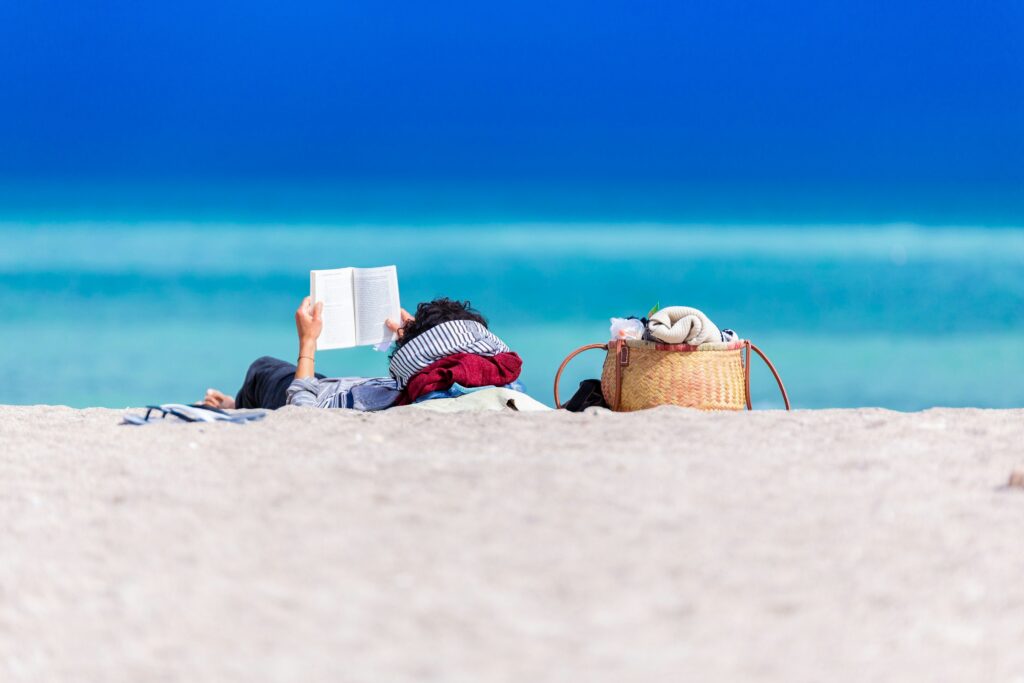 Millennial man relaxing on a beach and reading. Photo by Dan Dumitriu on Unsplash.